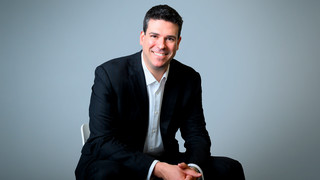 Headshot of 1998 alumnus Gregory Hayken in a black suit jacket and white-collared shirt