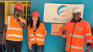 Alum Yasmine Karam, center, and colleagues wearing hard hats stand outside the BioMassters factory in northern Rwanda.