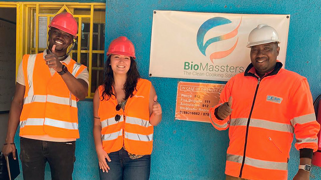 Alum Yasmine Karam, center, and colleagues wearing hard hats stand outside the BioMassters factory in northern Rwanda.