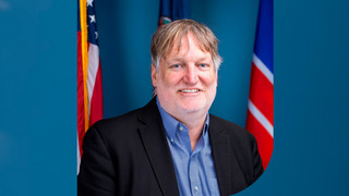 Headshot of Dr. Thad Williamson with flags on both sides