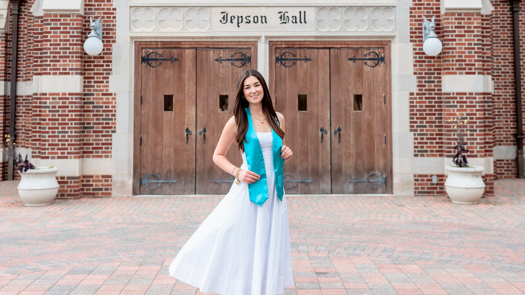 Emerson Linden, '26, in her white graduation dress and teal stole outside Jepson Hall