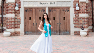 Emerson Linden, '26, in her white graduation dress and teal stole outside Jepson Hall