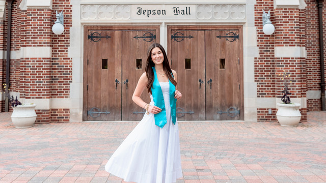 Emerson Linden, '26, in her white graduation dress and teal stole outside Jepson Hall