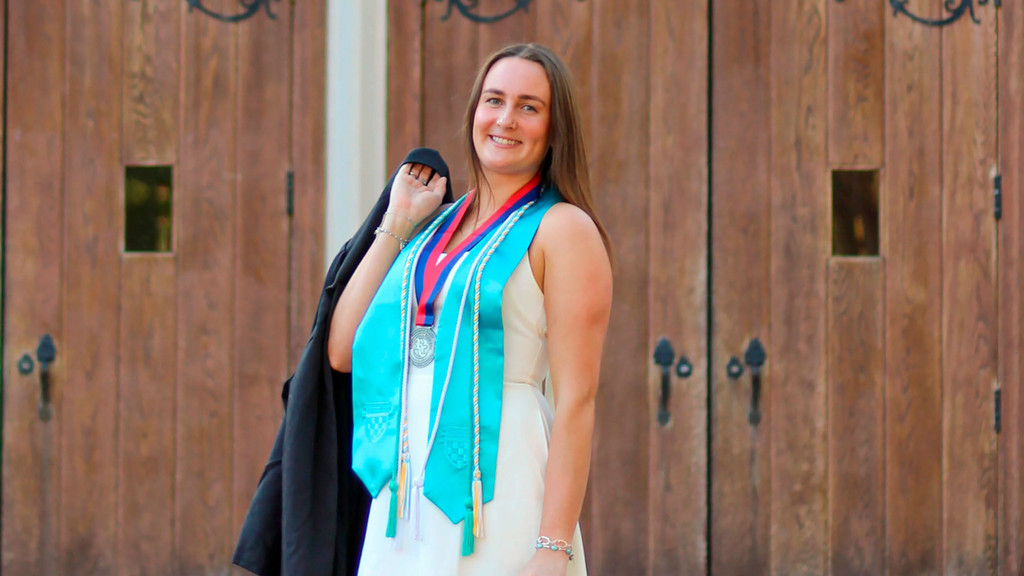 Senior Emma McCauley in a white dress adorned with her graduation stole and cords and her Richmond College Medal