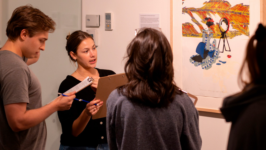 A photo of 3 people discussing a piece of art.