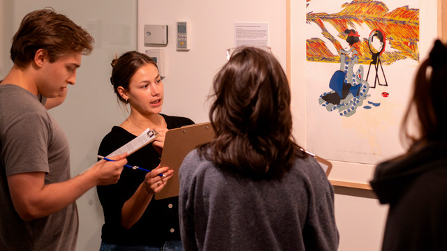 A photo of 3 people discussing a piece of art.