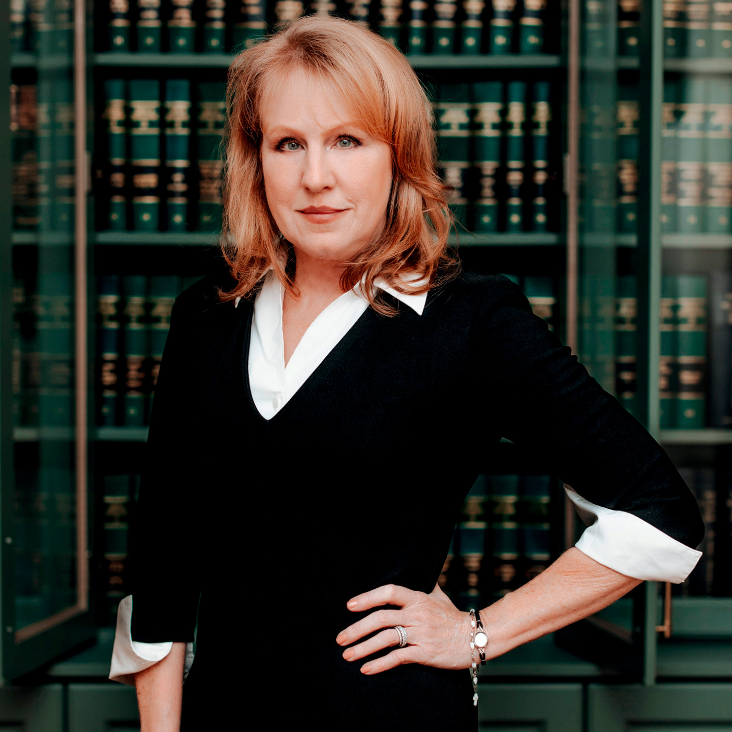 A portrait of Corinna Lain. She is looking at the camera and wearing a black suite and white shirt. She is posed in front of a library of law books.