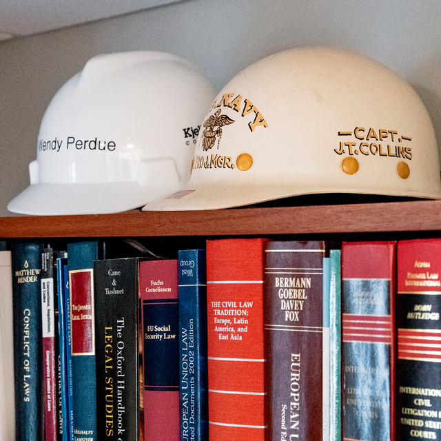 A photo of two hard hats on top of a bookshelf full of legal books. One hard had is labelled 