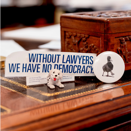 A photo of Dean Perdue's desk featuring a small ceramic Dalmation dog, holding a bumper sticker that reads 