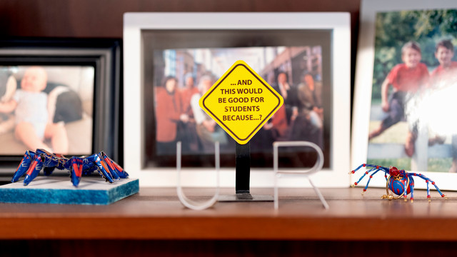 A photo of bookshelf in dean Perdue's office focused on a small yellow sign that reads 