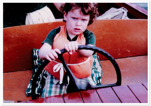 Dean Wendy Perdue as a small child, driving a boat. She has a serious look on her face.