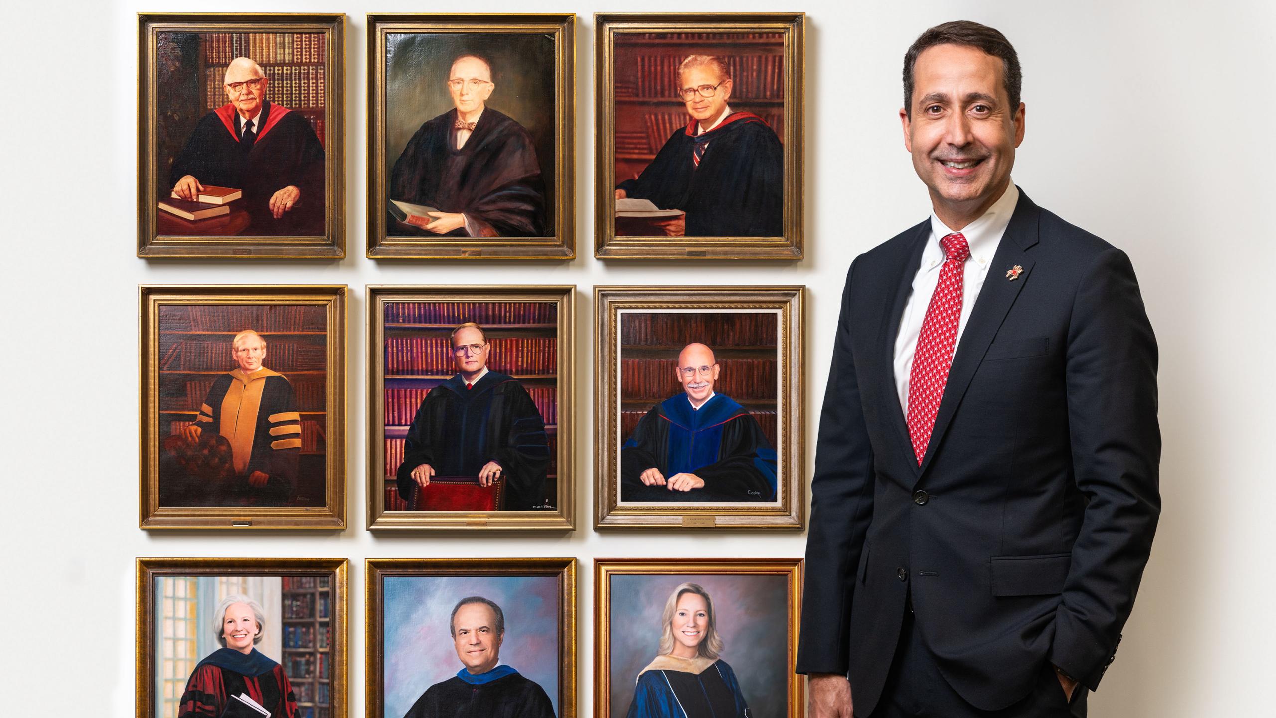 Dr. Mickey Quiñones,  Dean and Professor of Management at the Robins School of Business, stands with portraits of previous deans.
