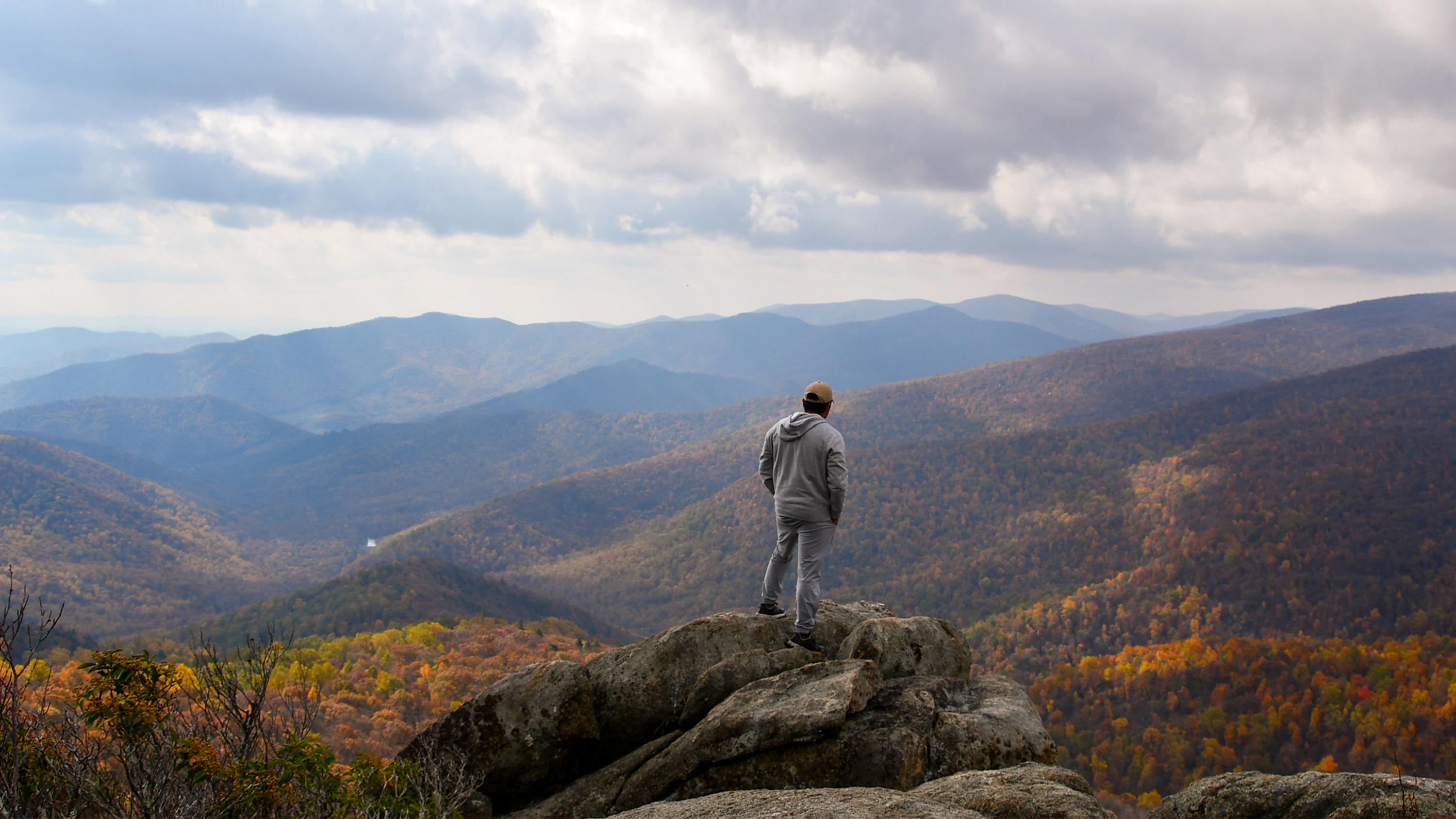 A photo of a person standing looking out at mountains and trees.