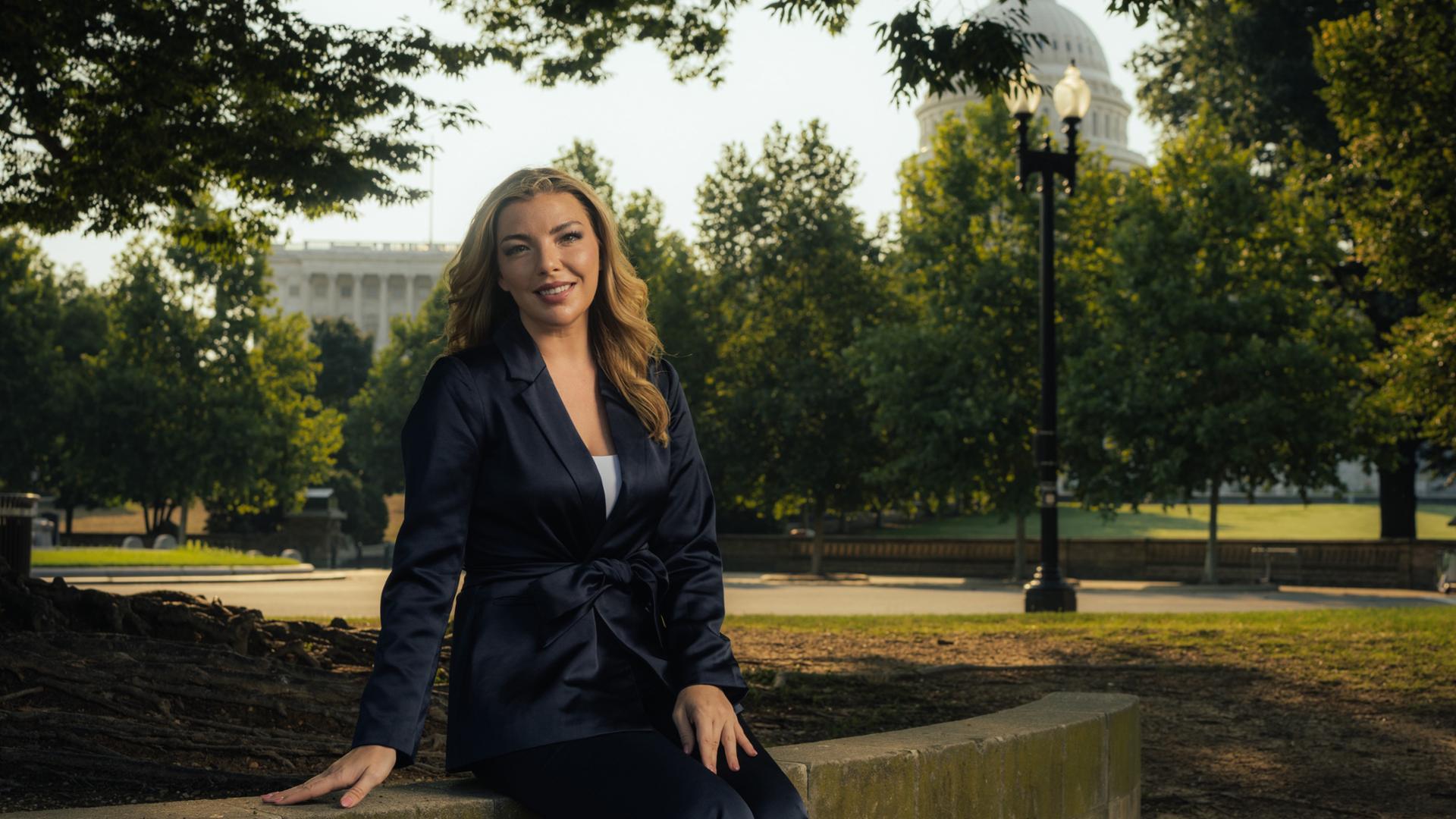 A photo of Molly Rossi, '16, sitting outside on the mall in Washington D.C.  She is surrounded by trees and the U.S. Capitol Dome is visible in the background.