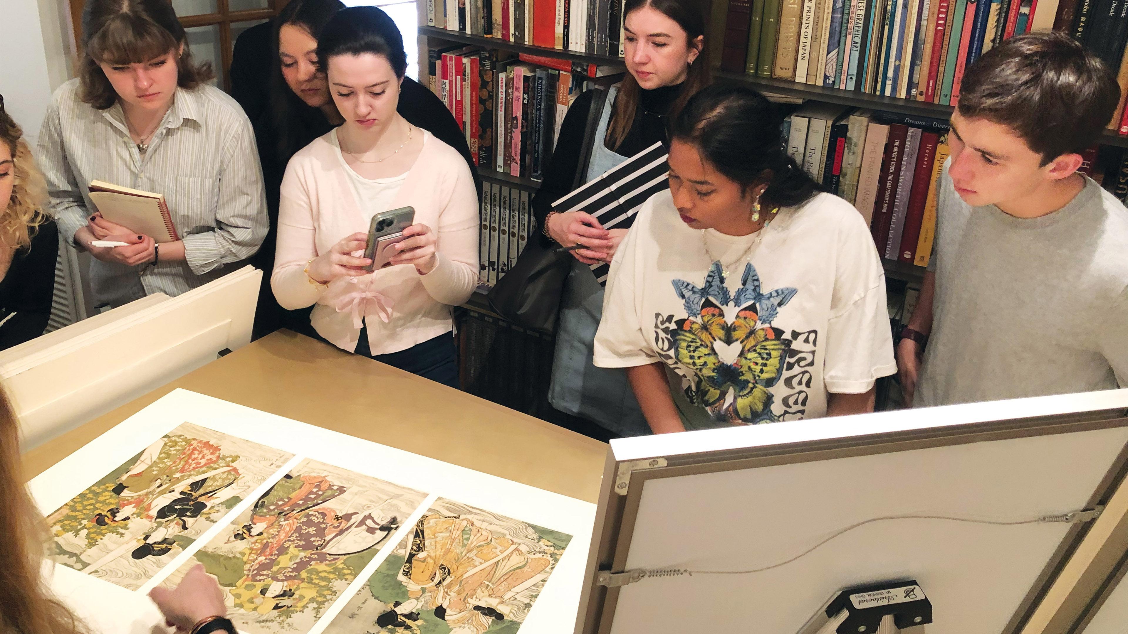 A group of students stand around Japanese woodblock prints.