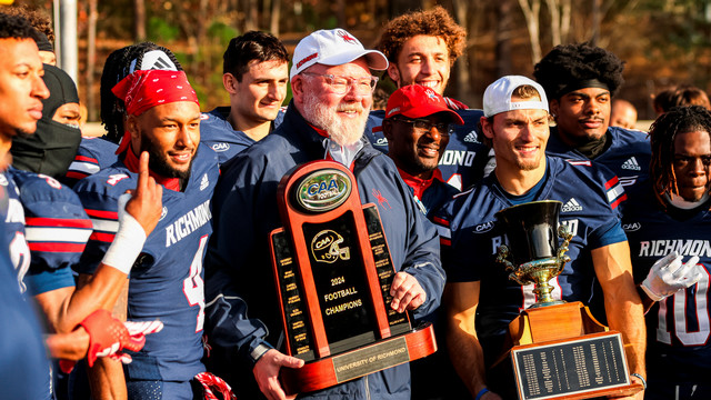 Athletics director John Hardt, with members of the football team, holding their CAA championship and Capital Cup trophies