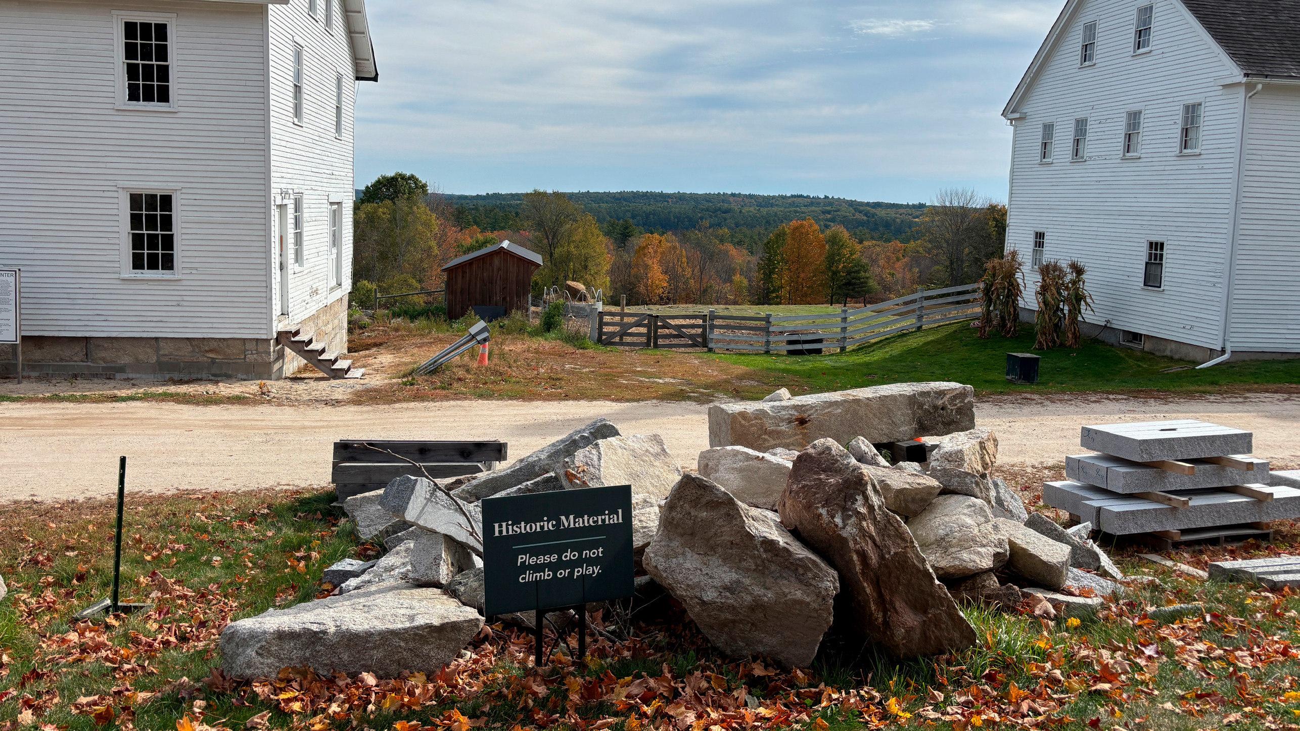 A landscape of the Shaker Village. A pile of stones sit with a sign saying 