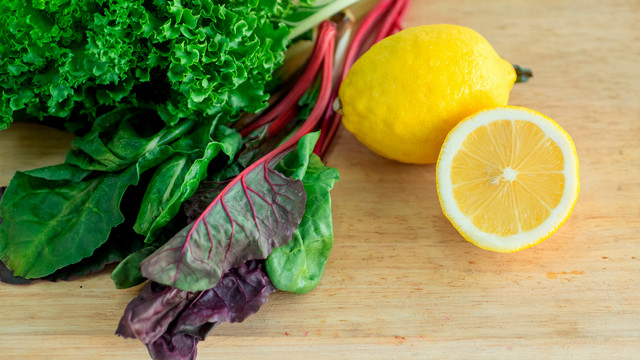 A photo of a pile pf dark leafy greens on a cutting board with lemons sitting next to them.