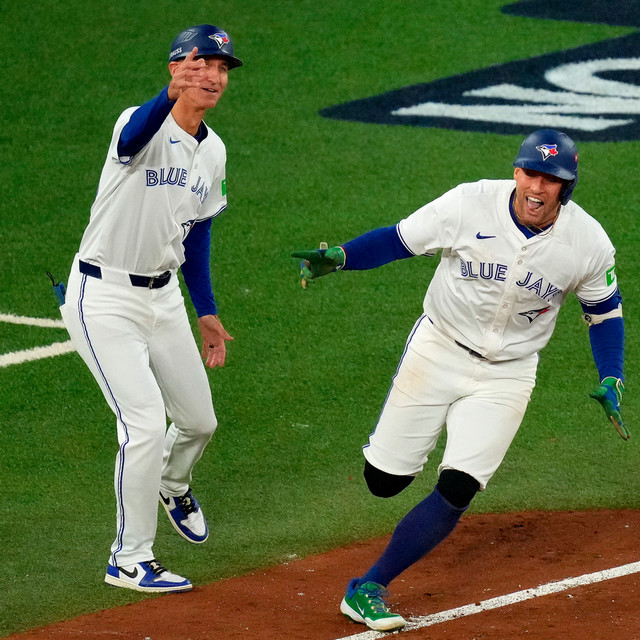 Toronto Blue Jays first base coach Mark Budzinski, left, cheers on George Springer, right, who rounds the bases after hitting a three-run home run against the Seattle Mariners during the seventh inning in Game 7 of baseball's American League Championship Series in Toronto, Monday, Oct. 20, 2025.