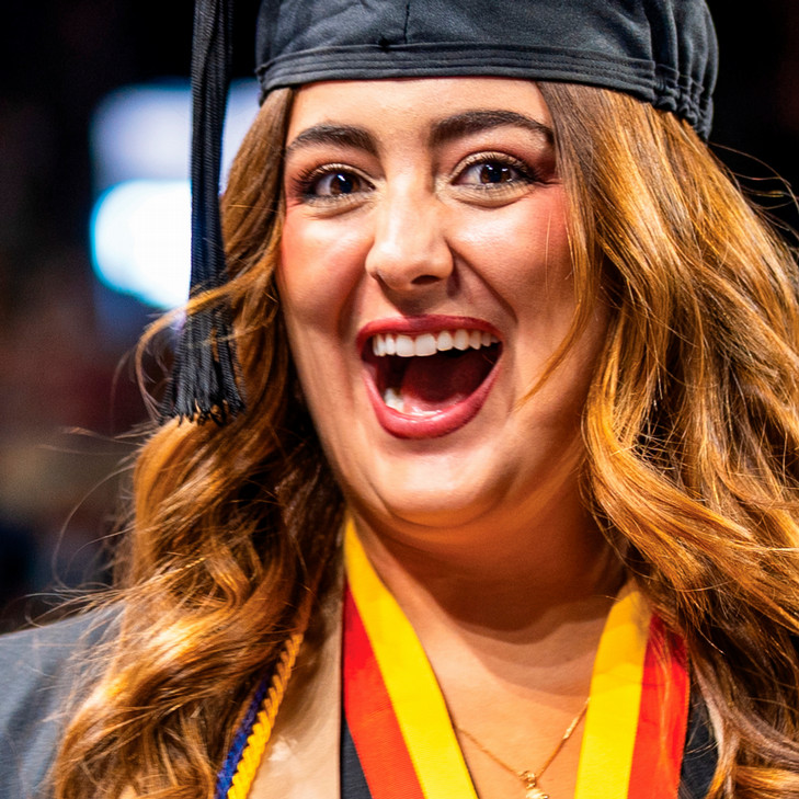 A student smiling with her mouth open. She is wearing a graduation mortarboard and gown.