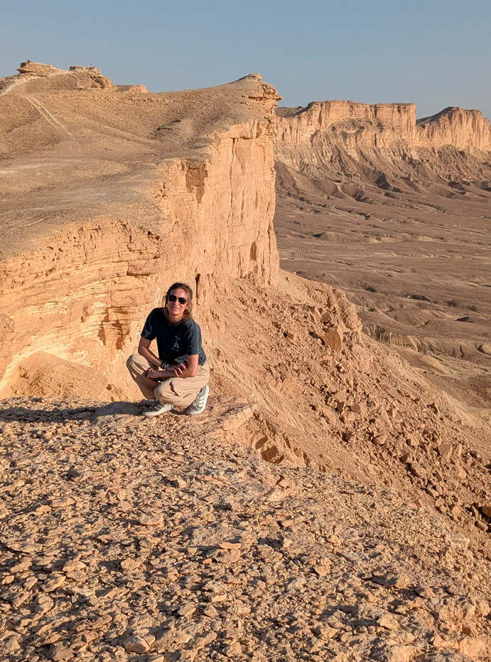 Katie Fishman kneels in the desert of Saudi Arabia.