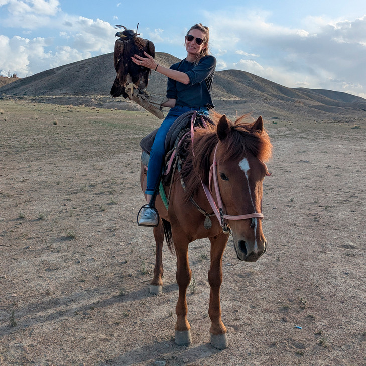 Katie Fishman rides a horse while holding an eagle on her arm in Kyrgyzstan.