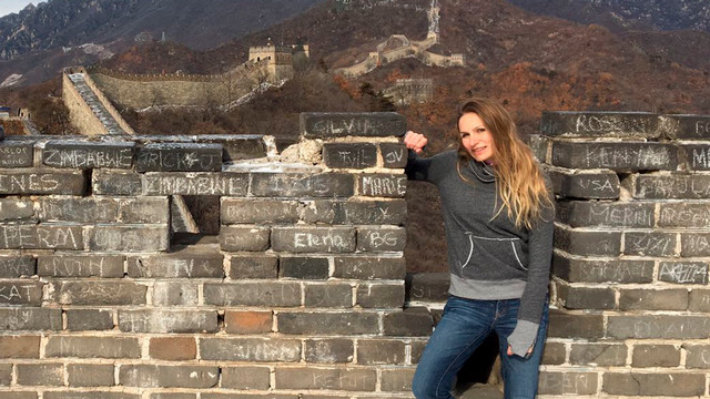 Katie Fishman stands on the Great Wall of China with the wall seen behind her.