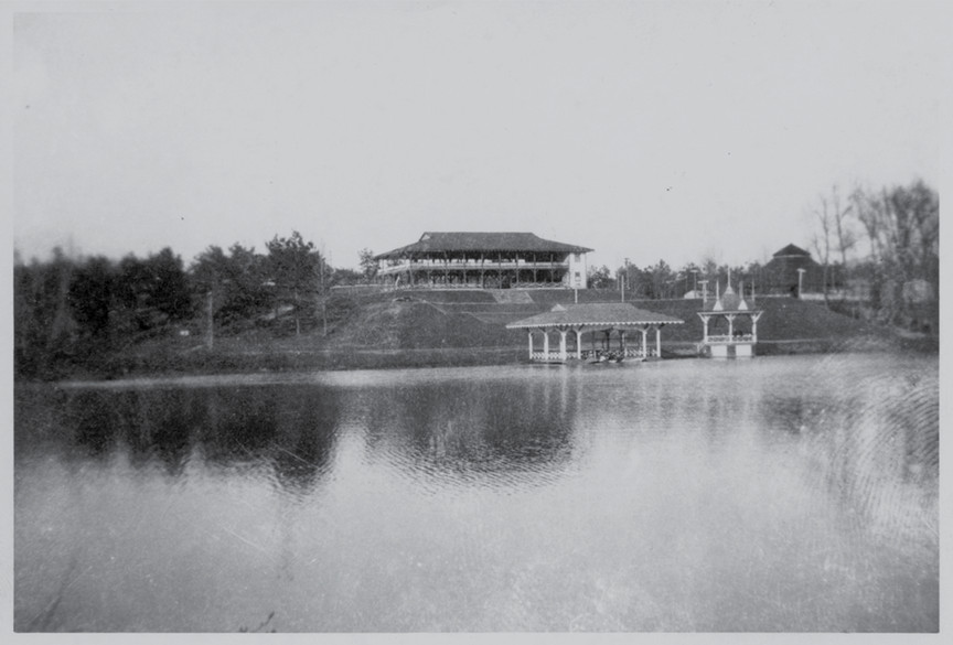 An historic photo of Westhampton Lake. The photo is in black and white and shows the pavilion that stood where Boatwright library now stands, and boathouse and landing on the nearby shore.