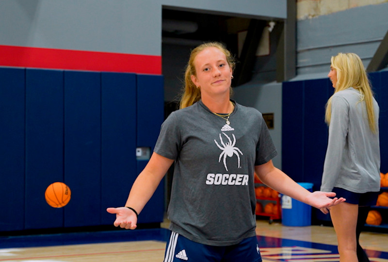 Marisa Snee shrugs at the camera as a basketball rolls off into the distance behind her. Spider women's basketball player Annika Manthy smiles in the background.
