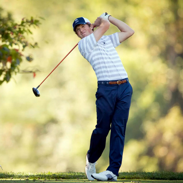 A photo of Daniel Walker in 2013. He is swinging a golf club on a golf course and wearing a white and blue striped Spiders golf shirt.
