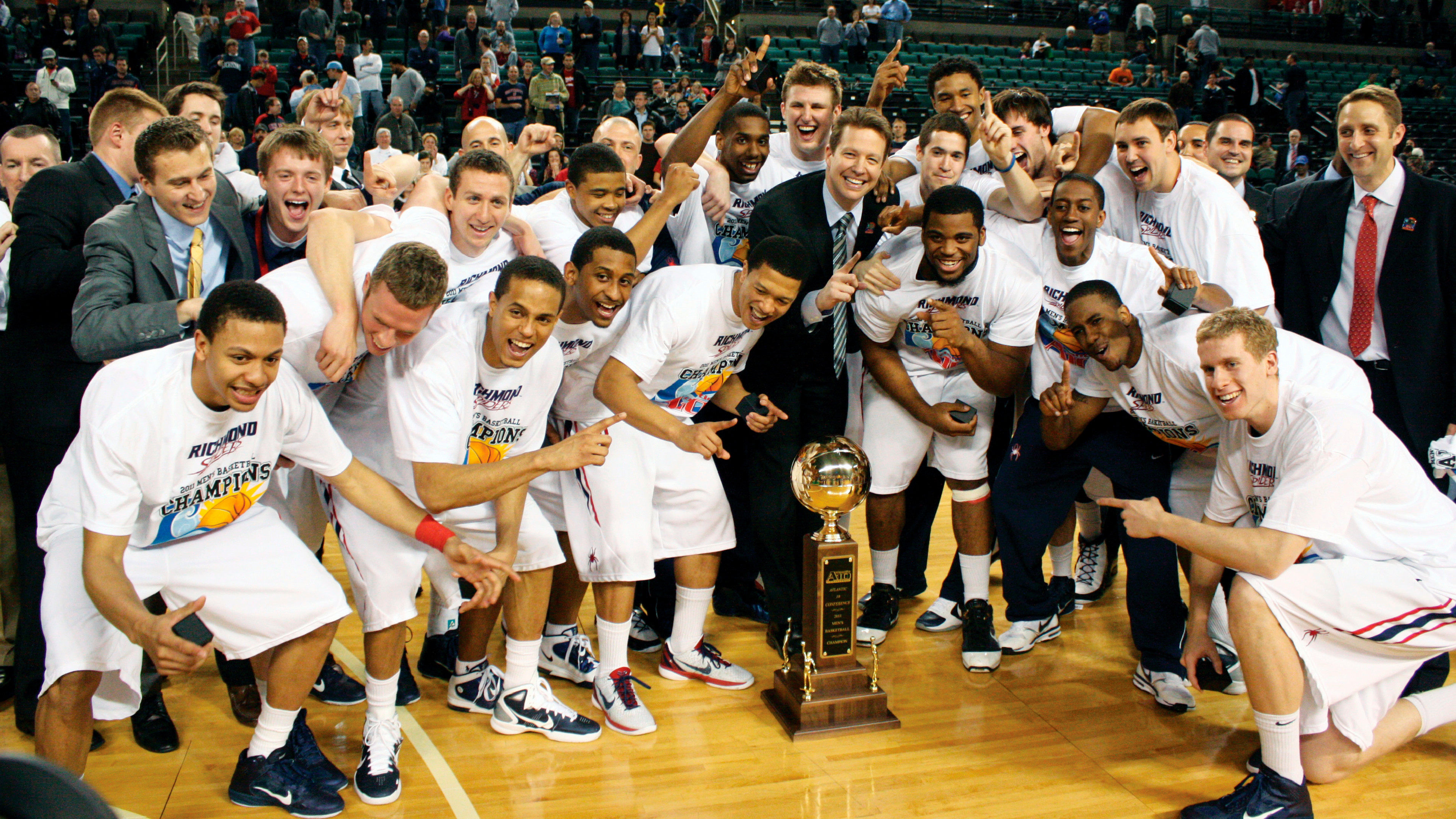 The 2011 university of richmond men's basketball team poses on the court with the A-10 trophy with coach Chris Mooney, center.