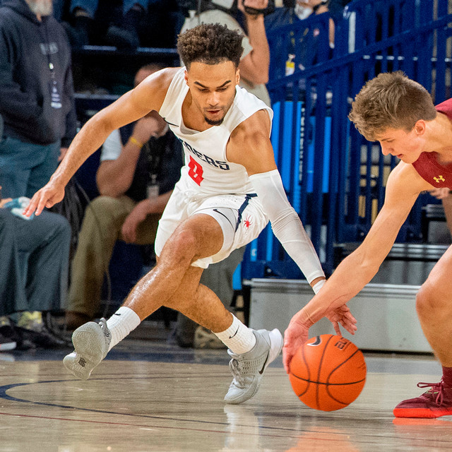 Jacob Gilyard stealing the basketball from an opponent. He wears a white Spider men's basketball uniform with number 0.