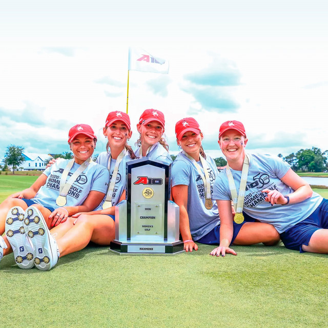 The University of Richmond women's golf team sitting on the golf course posing with the 2026 A-10 championship trophy.