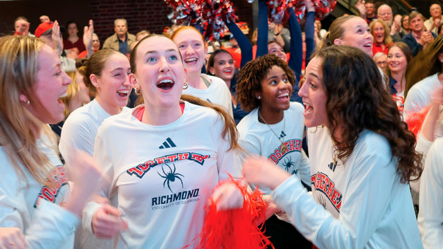 The University of Richmond women's basketball team celebrates the announcement that they would play in the NCAA tournament. They are jumping up and down and smiling.
