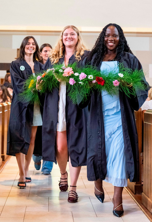Four Westhampton College students in dresses and graduation robes carrying a flowery garland through Cannon Memorial Chapel