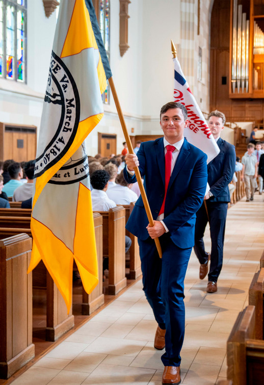 Two Richmond College students in blue suits and red ties carrying flags down the center aisle of Cannon Memorial Chapel