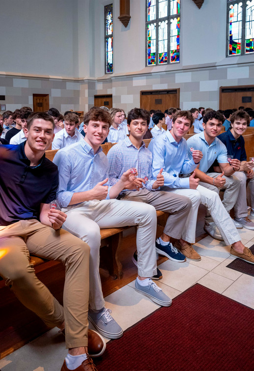 Row of six smiling Richmond College students wearing button-up shirts and sitting on a pew in Cannon Memorial Chapel while looking at the camera. Several give thumbs up.