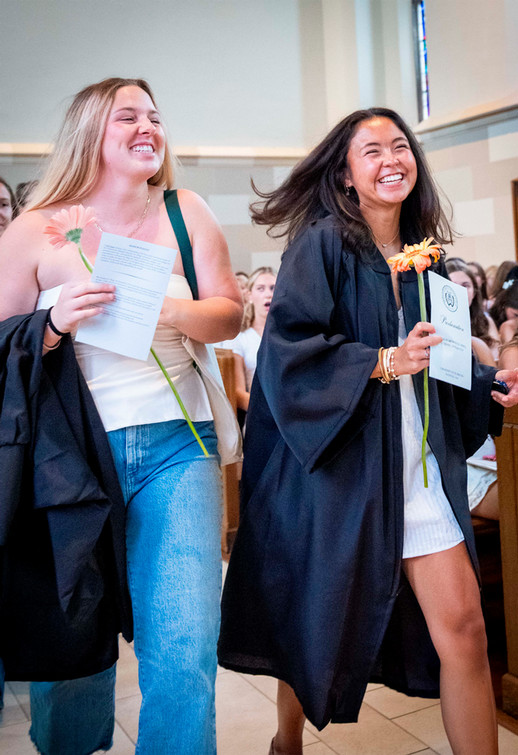 Two smiling Westhampton College students walk confidently through Cannon Memorial Chapel. One wears a black graduation robe. The other has her robe slung across her arm.