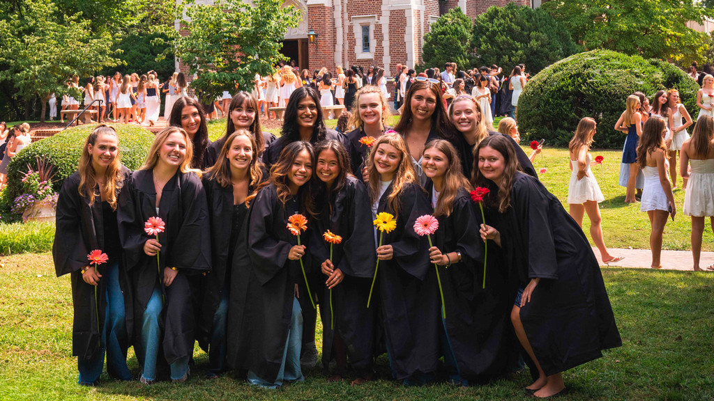 More than a dozen Westhampton students posing together in black graduation robes and holding flowers in front of Cannon Chapel following Proclamation 2026