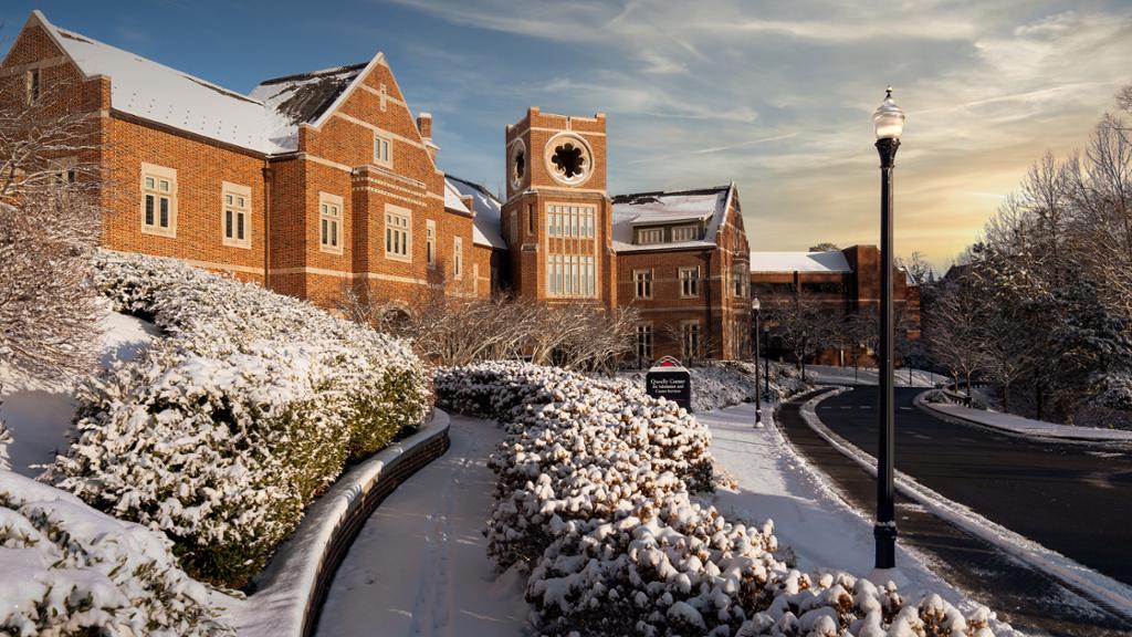 Large brick building with a tower, covered in a light snow