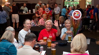 People seated at round tables, talking with one another and drinking from glasses of beer, wine and soda