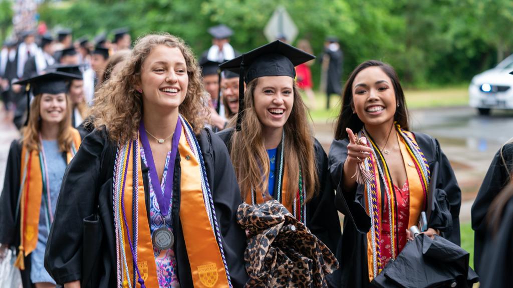 Richmond graduates wearing caps and gowns walk across campus at Commencement.