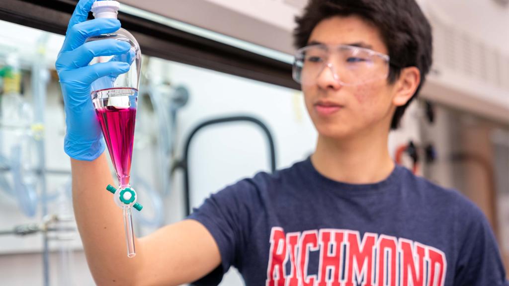 Chemistry student wearing safety goggles and holding a piece of lab equipment.