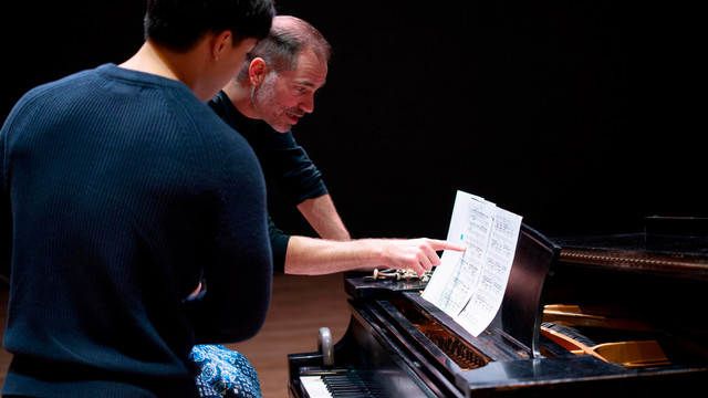 a music alumnus points out a passage of music to a student during a vocal masterclass