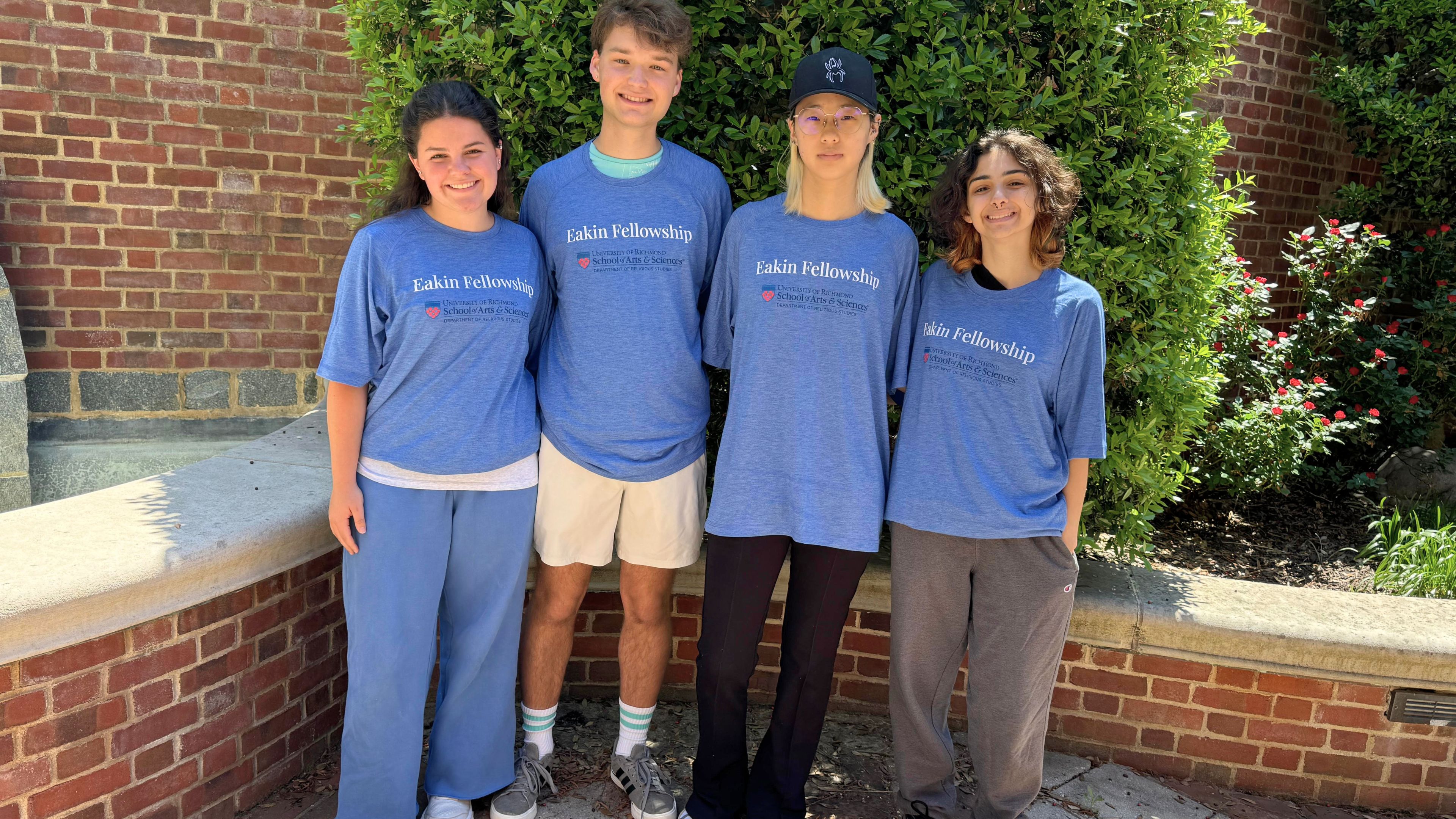 Photo of 4 students smiling outside wearing blue Eakin Fellowship t-shirts