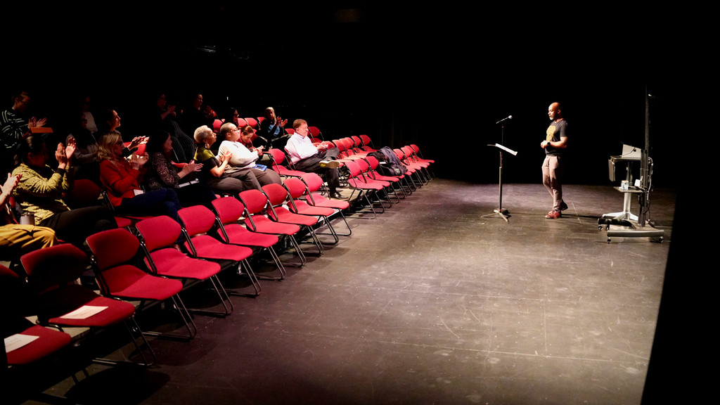 spoken word artist performs to a crowd in a black box theater