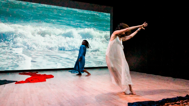 a modern dance performance by two dancers in front of a video projection of ocean waves