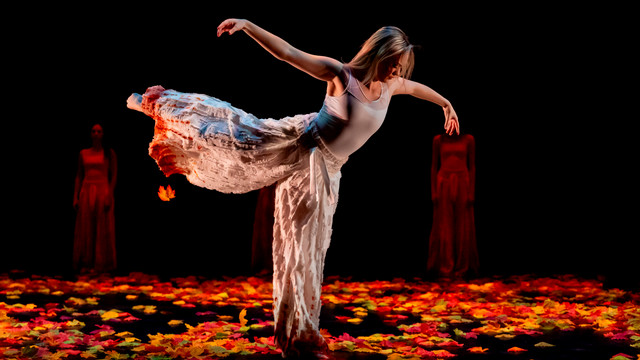 student dancer in a dramatic pose looking down at the stage covered in autumn leaves