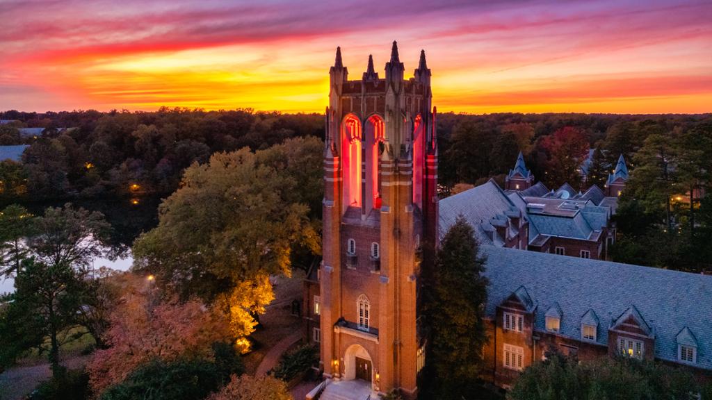 Aerial view of Boatwright tower illuminated red in front of a bright pink and orange sunset.