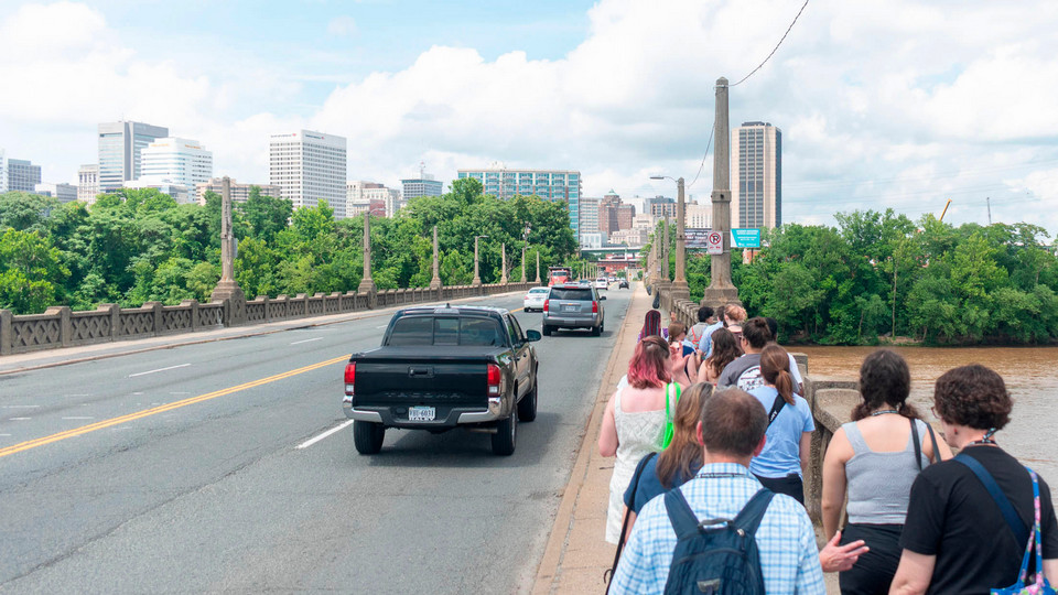 A group of Bonner scholars walking across the Mayo bridge in downtown Richmond. There are tall buildings visible in the distance.